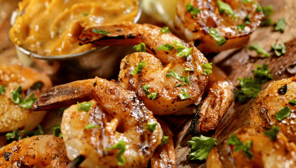 Knusprig gegrillte Garnelenspieße mit frischer Petersilie und Dip auf einem Holzbrett nach dem erfolgreichen Garnelen marinieren